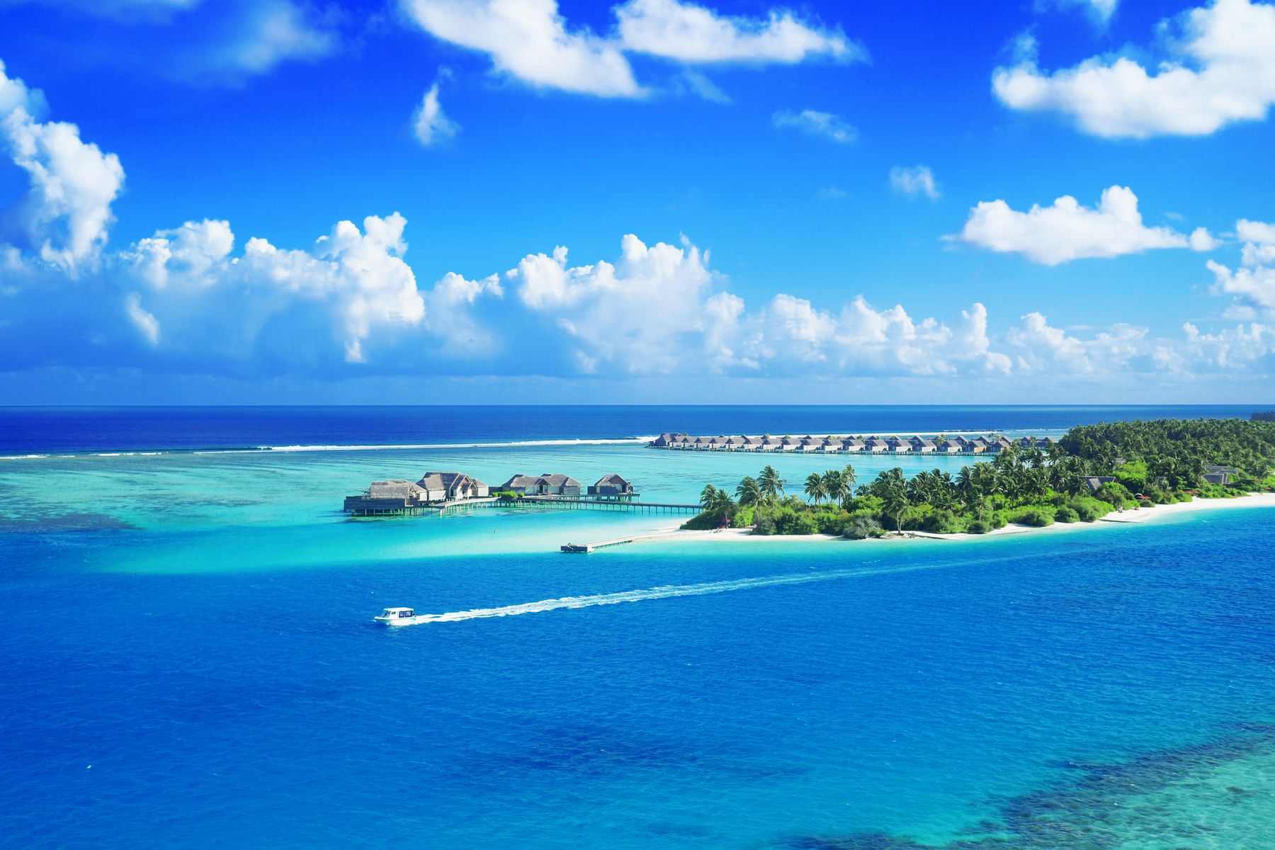 Aerial view of a Maldives resort with overwater villas over a turquoise lagoon